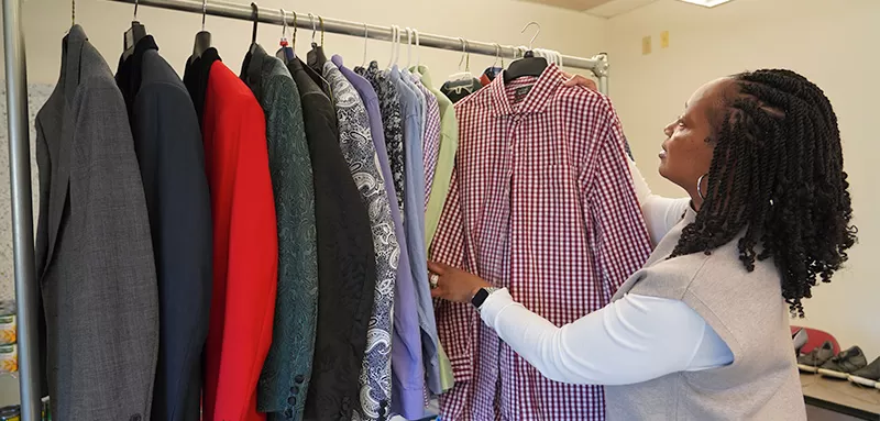 Picture of clothing and jackets on hangers hanging on a rack with a young lady adding an item to the rack.