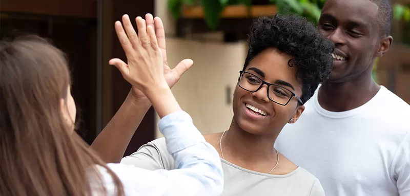 Cheerful african and caucasian young women standing outdoors in summer cafe greeting each other giving high five showing support and unity. 