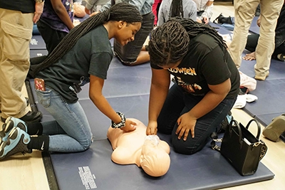 High school students practicing CPR chest compressions on a dummy.