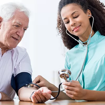 Young female nurse taking older patient blood pressure.